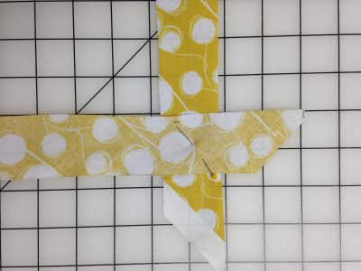 Two strips of yellow fabric with white dots, one laid facing down on the other at a 90 degree angle, pinned at the overlap