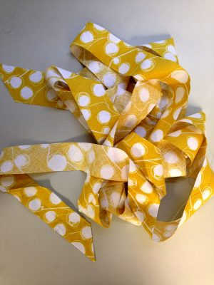 A length of bias tape, made in yellow fabric patterned with white dots