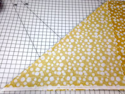Yellow fabric with white dots, folded diagonally on a cutting board