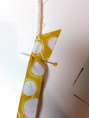 A strip of yellow fabric with white dots with piping cord coming from one end. A pin holds the piping cord in place.