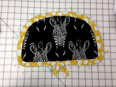 Yellow and white piping pinned to overlap at the bottom of a black bag panel patterned with zebra heads